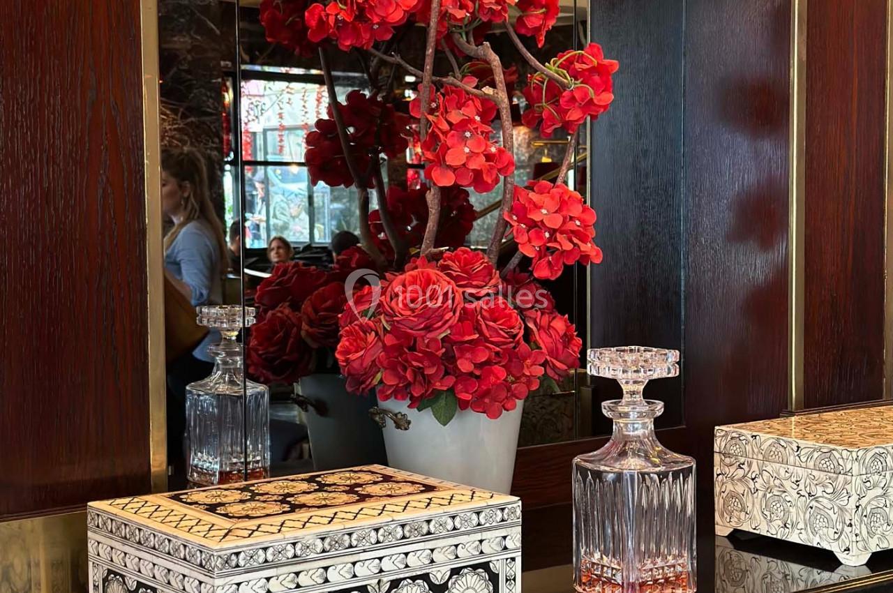 Vase de fleurs rouges avec des objets décoratifs en bois et en verre posés sur un meuble sombre.