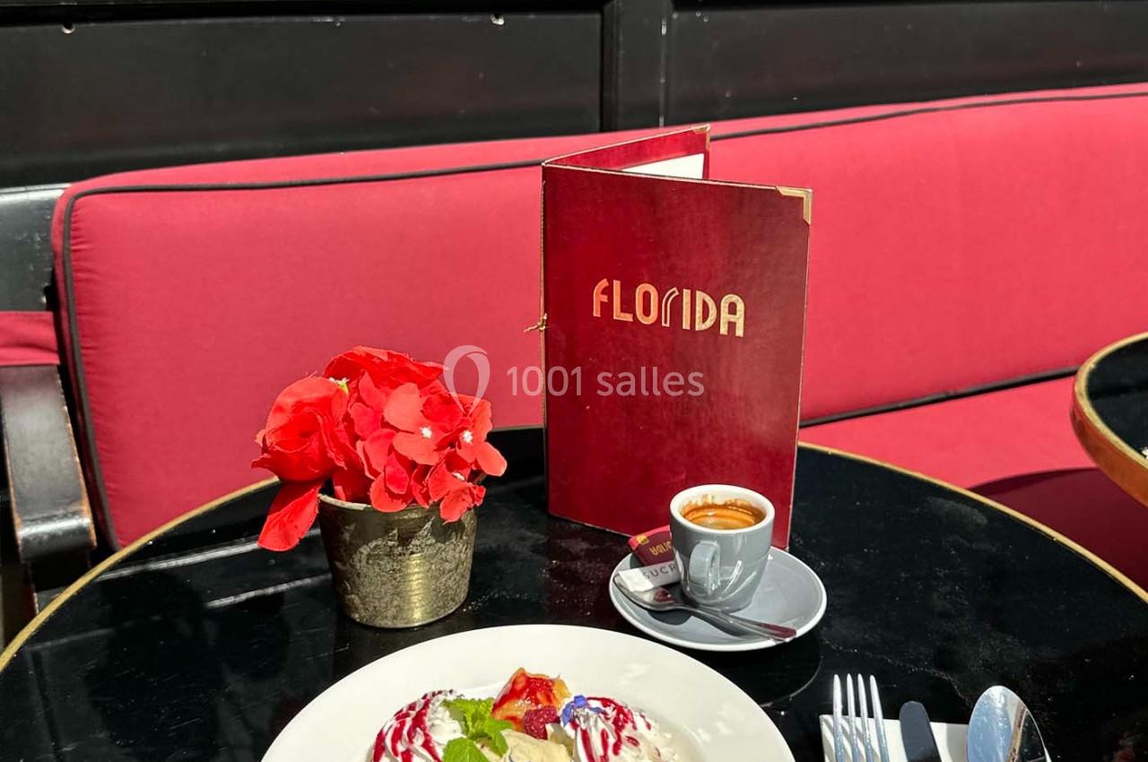 Dessert avec chantilly, fruits rouges et menthe, servi sur une terrasse avec un café, un menu et des fleurs rouges.