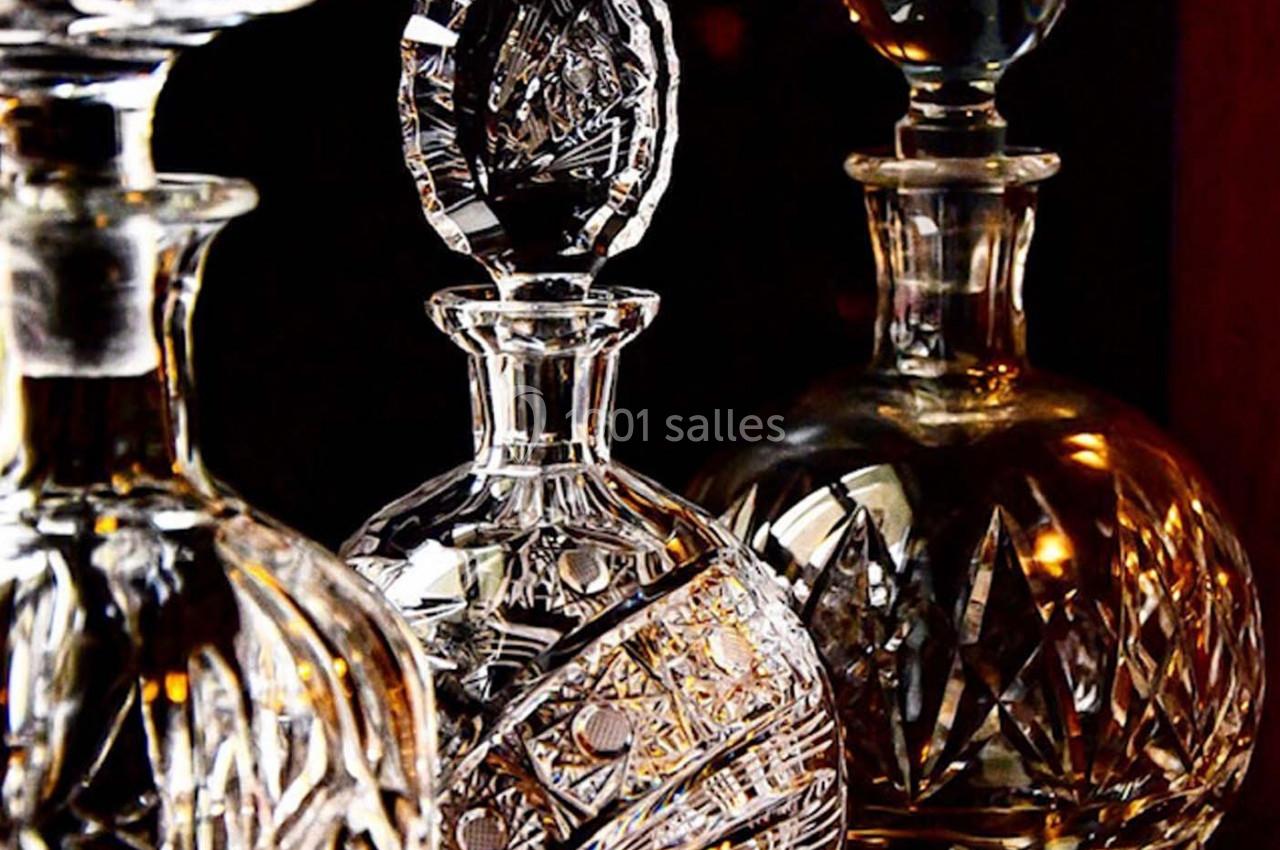 Trois carafes en cristal finement gravées, éclairées par une lumière chaude, posées sur une surface sombre.