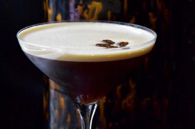 Verre à cocktail rempli d'un espresso martini, garni de grains de café, avec un fond sombre et texturé.