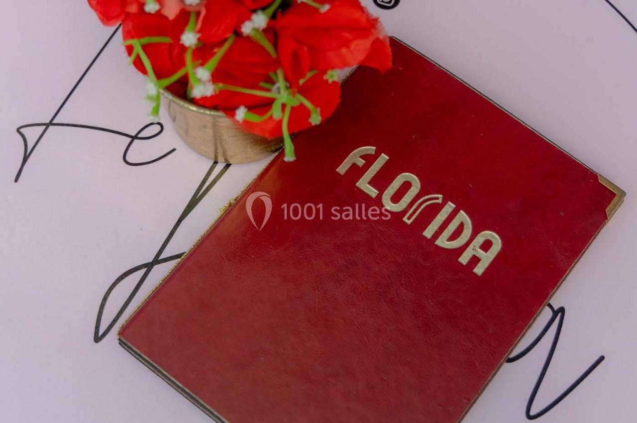 Menu rouge marqué ’Florida’ posé sur une table ronde blanche avec un bouquet de fleurs rouges et des QR codes imprimés.