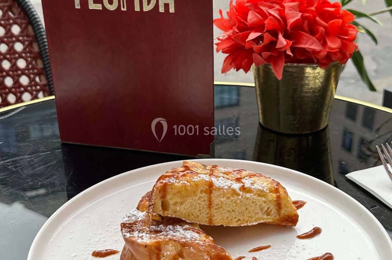 Assiette de pain perdu avec boule de glace et caramel, servie sur une table en terrasse avec un menu et une plante rouge.