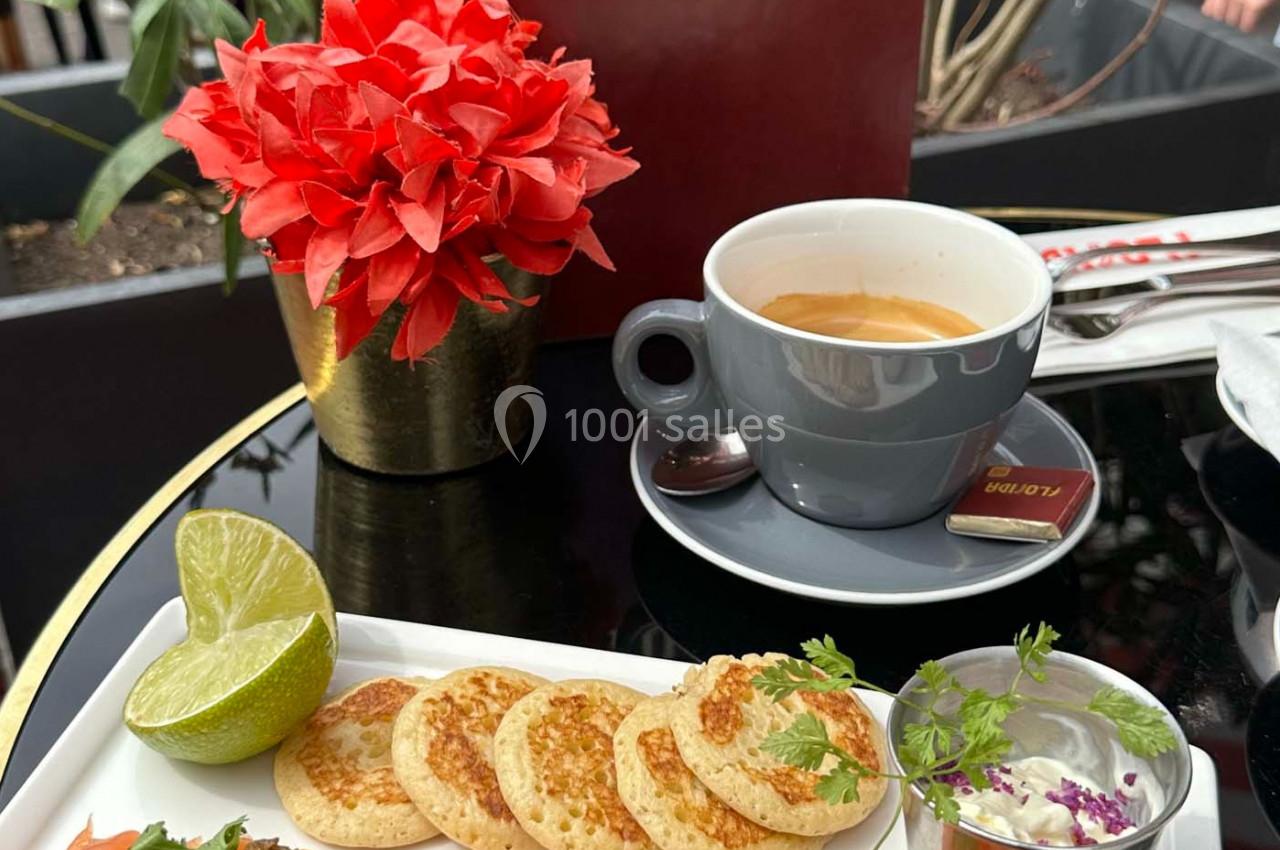 Assiette de saumon fumé, blinis, citron vert et crème, accompagnée d'un café sur une table de terrasse.