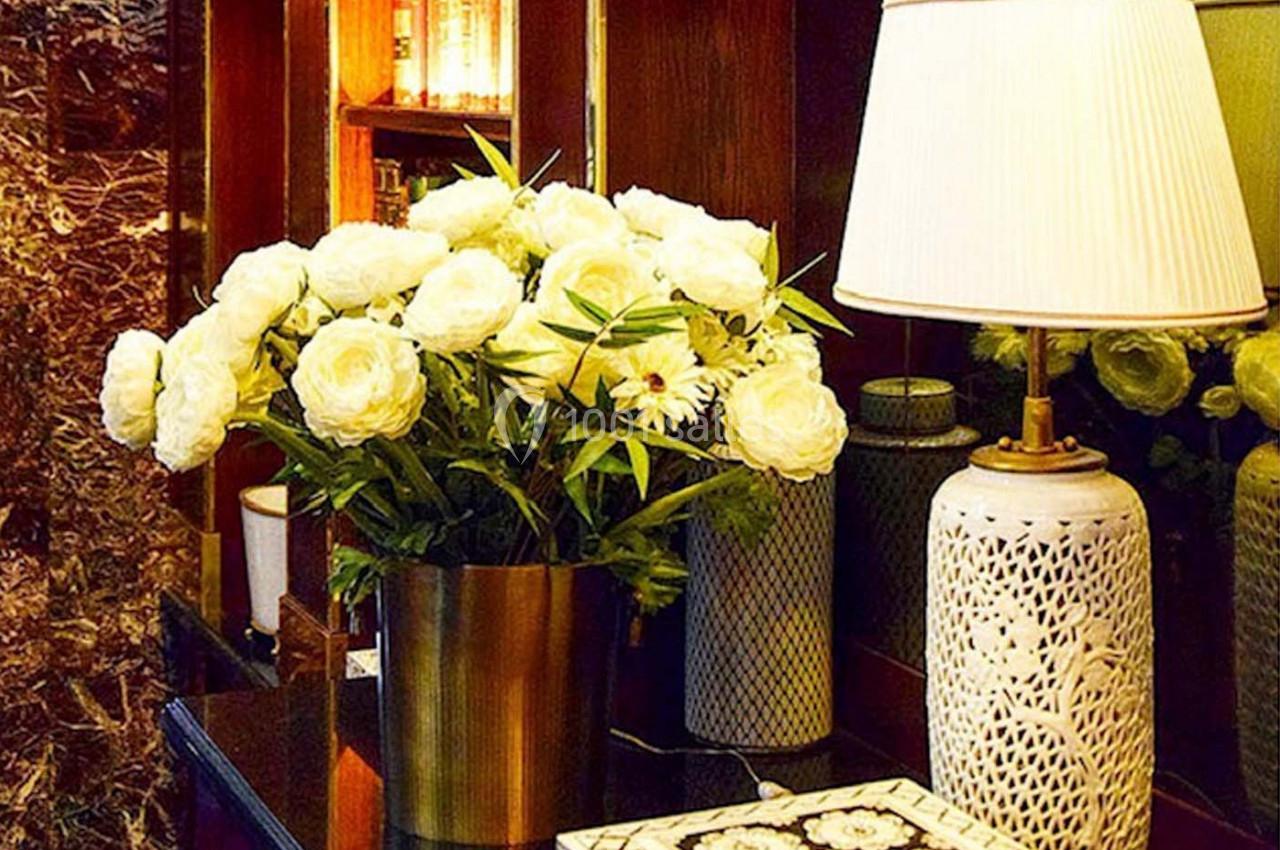 Bouquet de fleurs blanches dans un vase doré posé sur une table en bois, à côté d'une lampe et d'objets décoratifs.