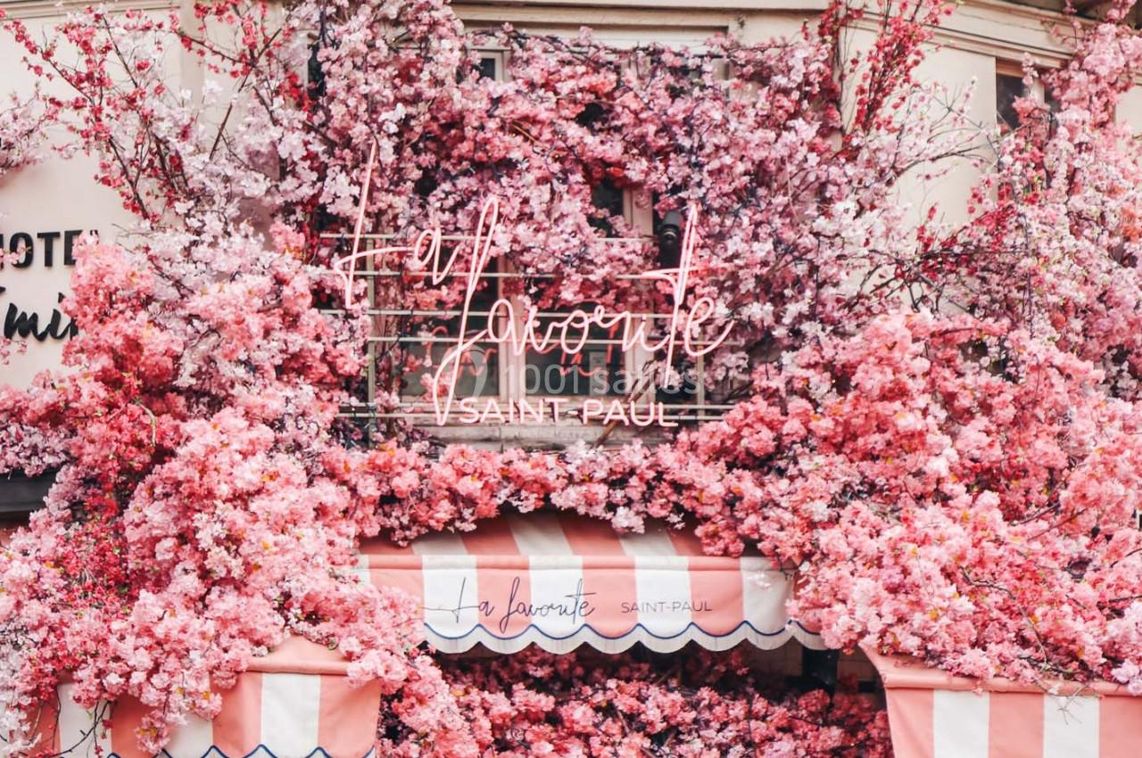 Façade d'une boutique ornée de fleurs roses et d'une enseigne lumineuse indiquant ’La Favorite Saint Paul’.