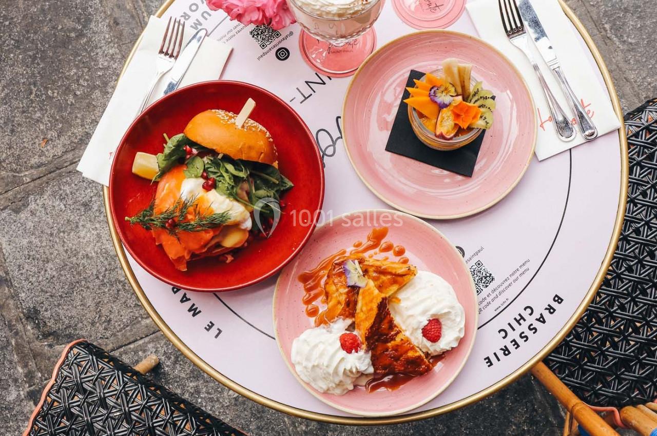 Assiette de burger avec salade, dessert à la chantilly et crêpes, servis sur une table ronde en extérieur.