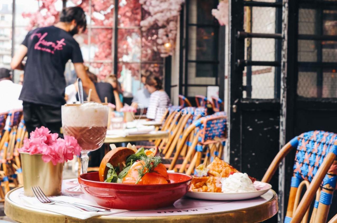 Repas servi en terrasse avec un bol de salade, une boisson et des fleurs roses en décoration sur la table.