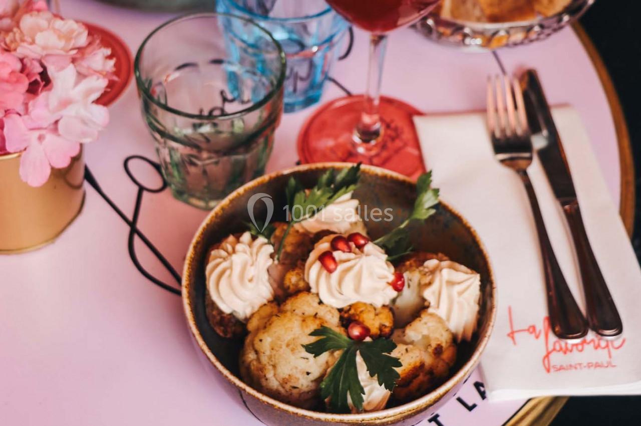 Bol de chou-fleur rôti garni de crème, graines de grenade et persil, posé sur une table avec couverts et verre.