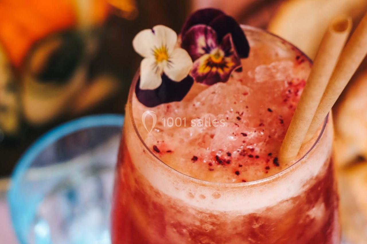 Boisson glacée rose garnie de fleurs comestibles et de pailles, servie dans un verre transparent.