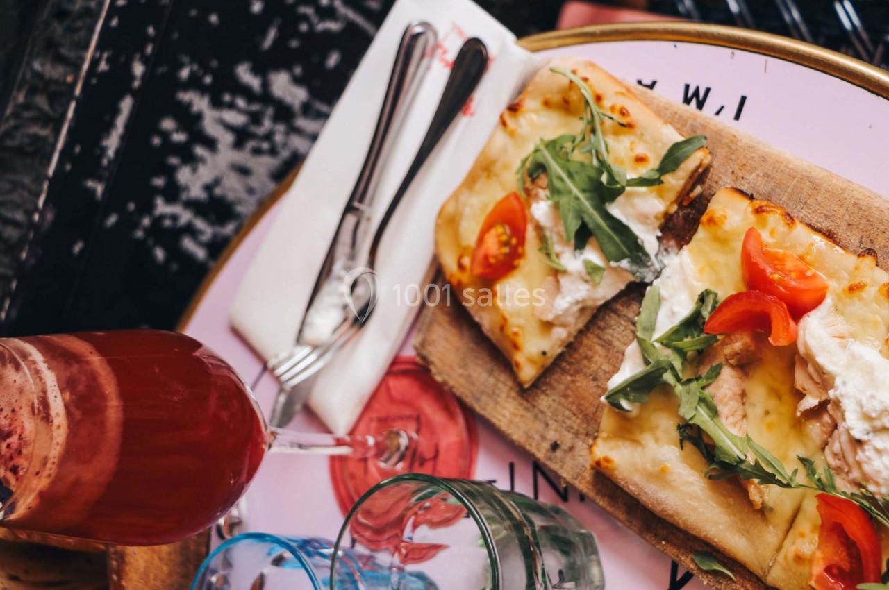 Deux parts de pizza garnies de roquette, tomates et fromage, servies sur une planche avec des couverts et un verre de…