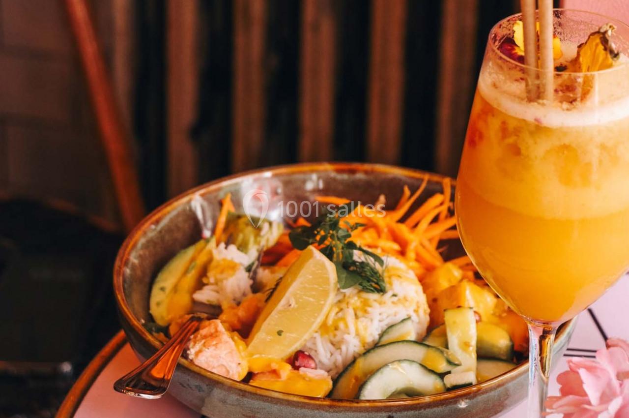 Bol de salade colorée avec légumes, riz, citron et herbes, accompagné d'un verre de jus orange garni de fruits.