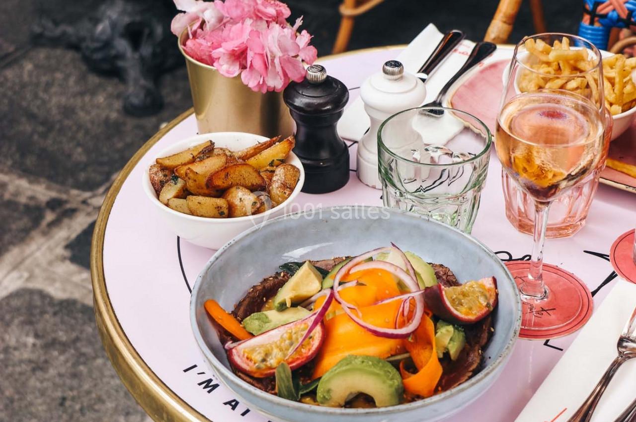 Assiette de salade colorée avec légumes et fruits, accompagnée de pommes de terre, frites et boissons sur une table.