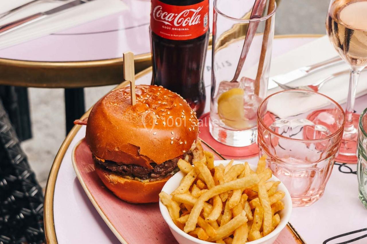Burger avec pain brioché, frites dans un bol, verre de vin rosé et bouteille de Coca-Cola sur une table de café.