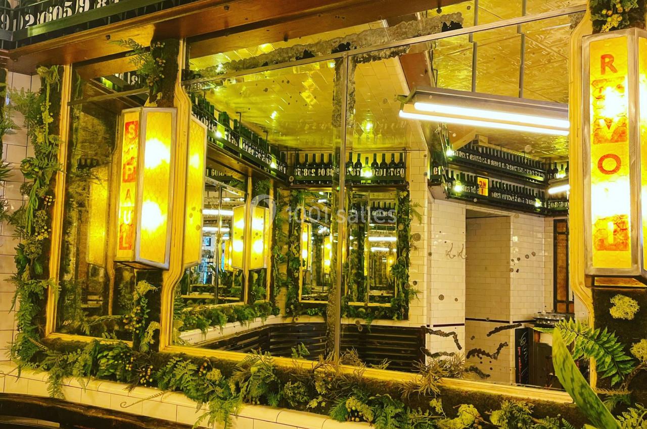 Miroirs encadrés de végétation et éclairés par des lampes jaunes, reflétant un décor intérieur lumineux.