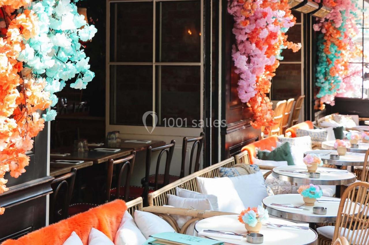 Salle de restaurant décorée de fleurs colorées avec des tables rondes et des chaises en bois et rotin.