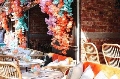 Étagères en bois remplies de bouteilles d'alcool, encadrées de briques et de feuillage, dans un décor de bar chaleureux.