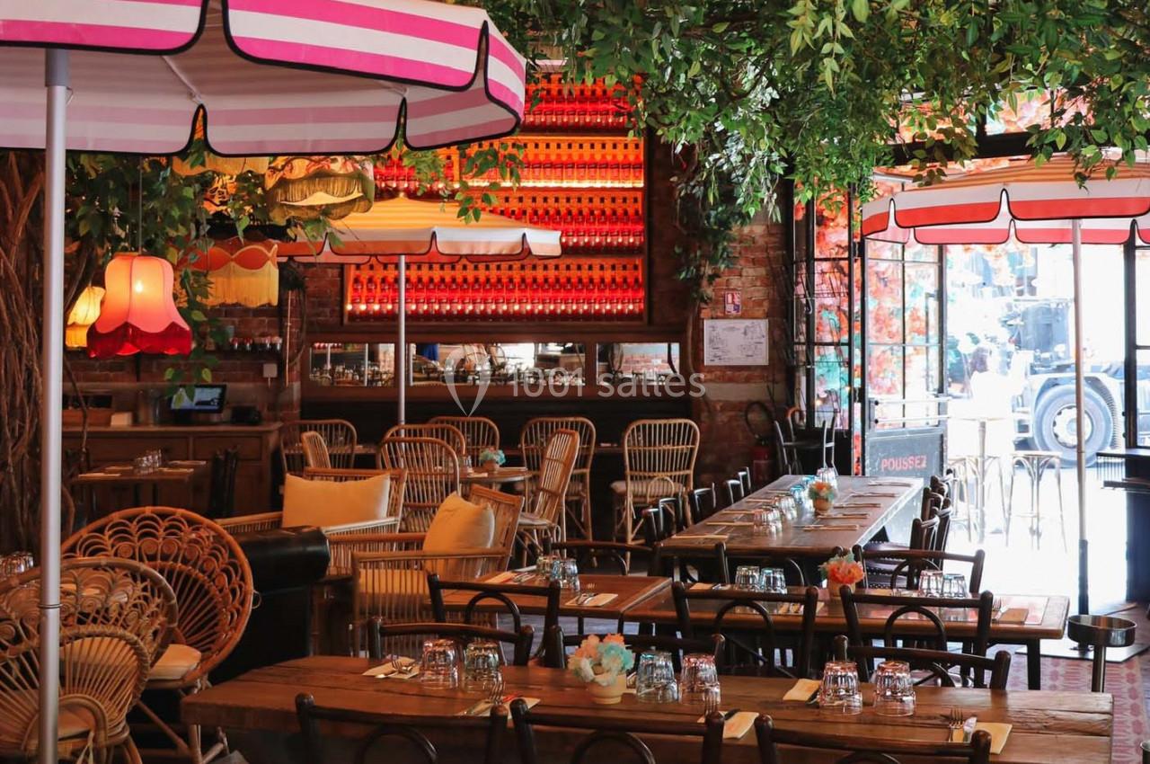 Salle de restaurant décorée avec des plantes suspendues, des lampes colorées et des tables en bois dressées.