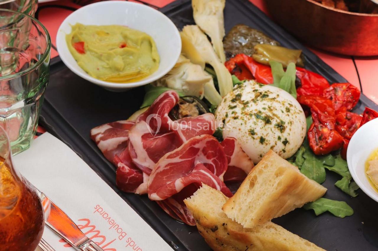 Assiette composée de burrata, charcuterie, légumes grillés, pain et guacamole, servie sur un plateau noir.