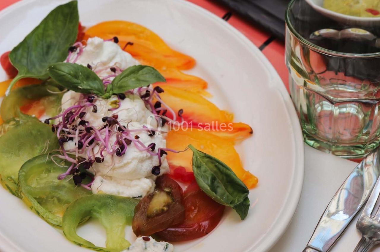 Assiette de salade colorée avec tomates variées, burrata, pousses germées et feuilles de basilic.