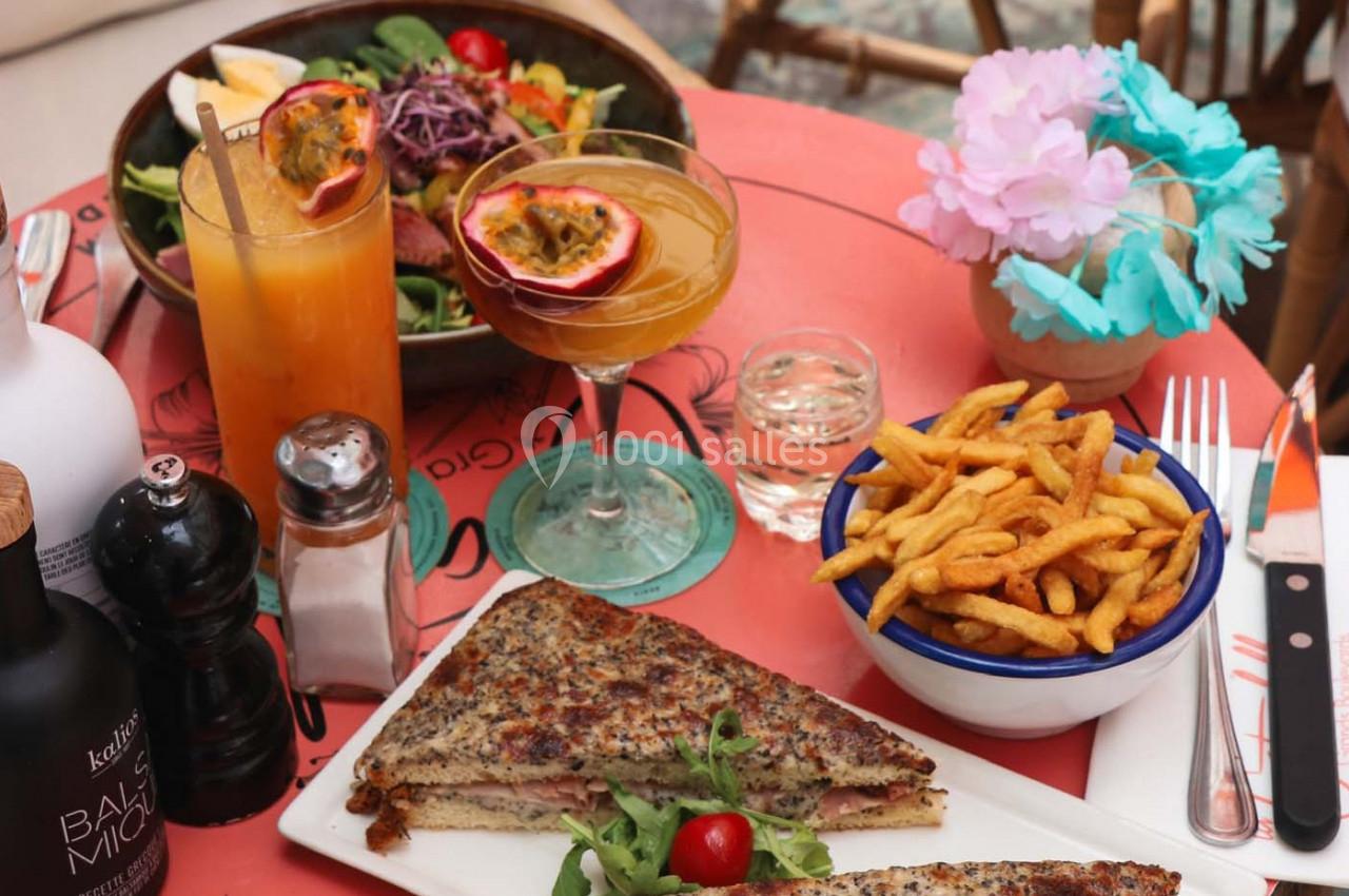 Assiette de croque-monsieur, frites, cocktails et salade sur une table colorée avec décorations florales.