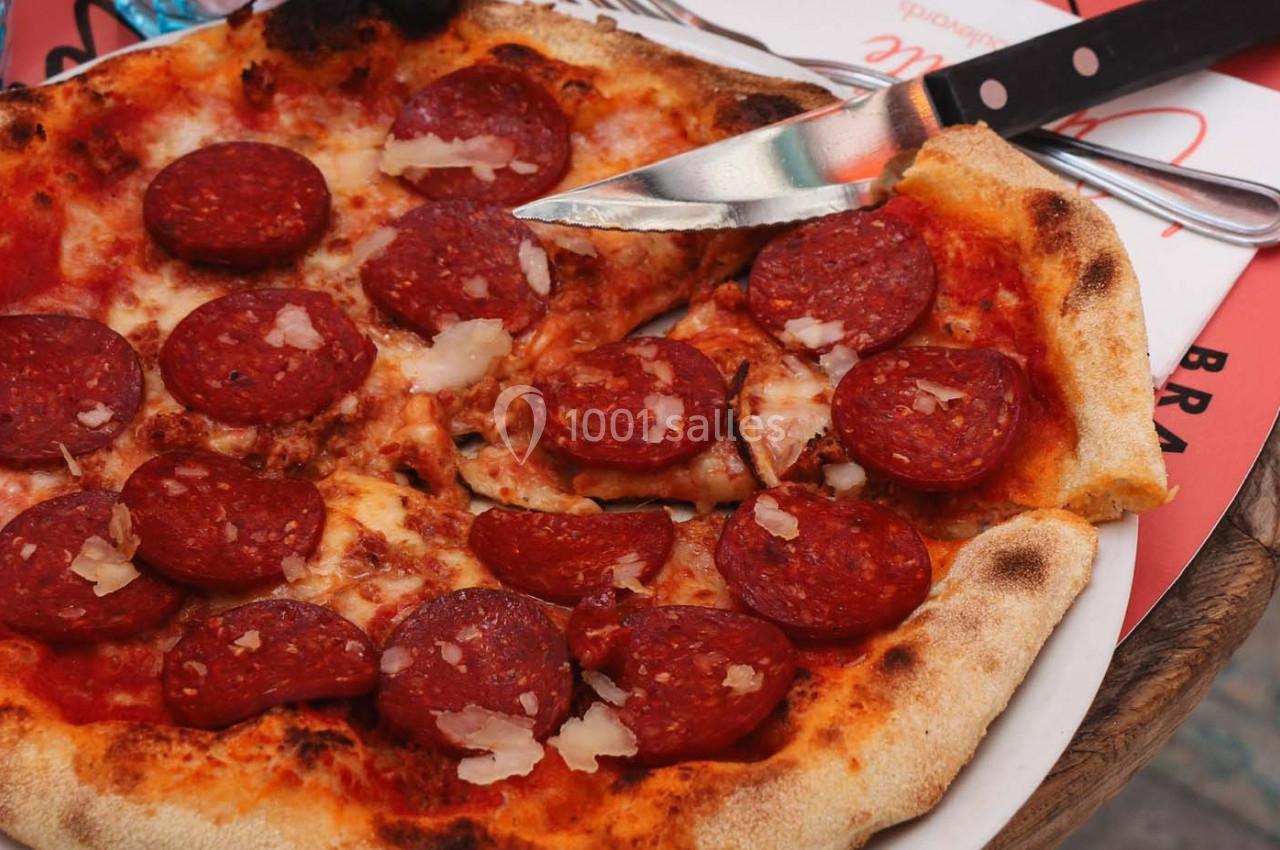 Pizza au pepperoni avec fromage râpé, servie sur une assiette blanche avec un couteau posé à côté.