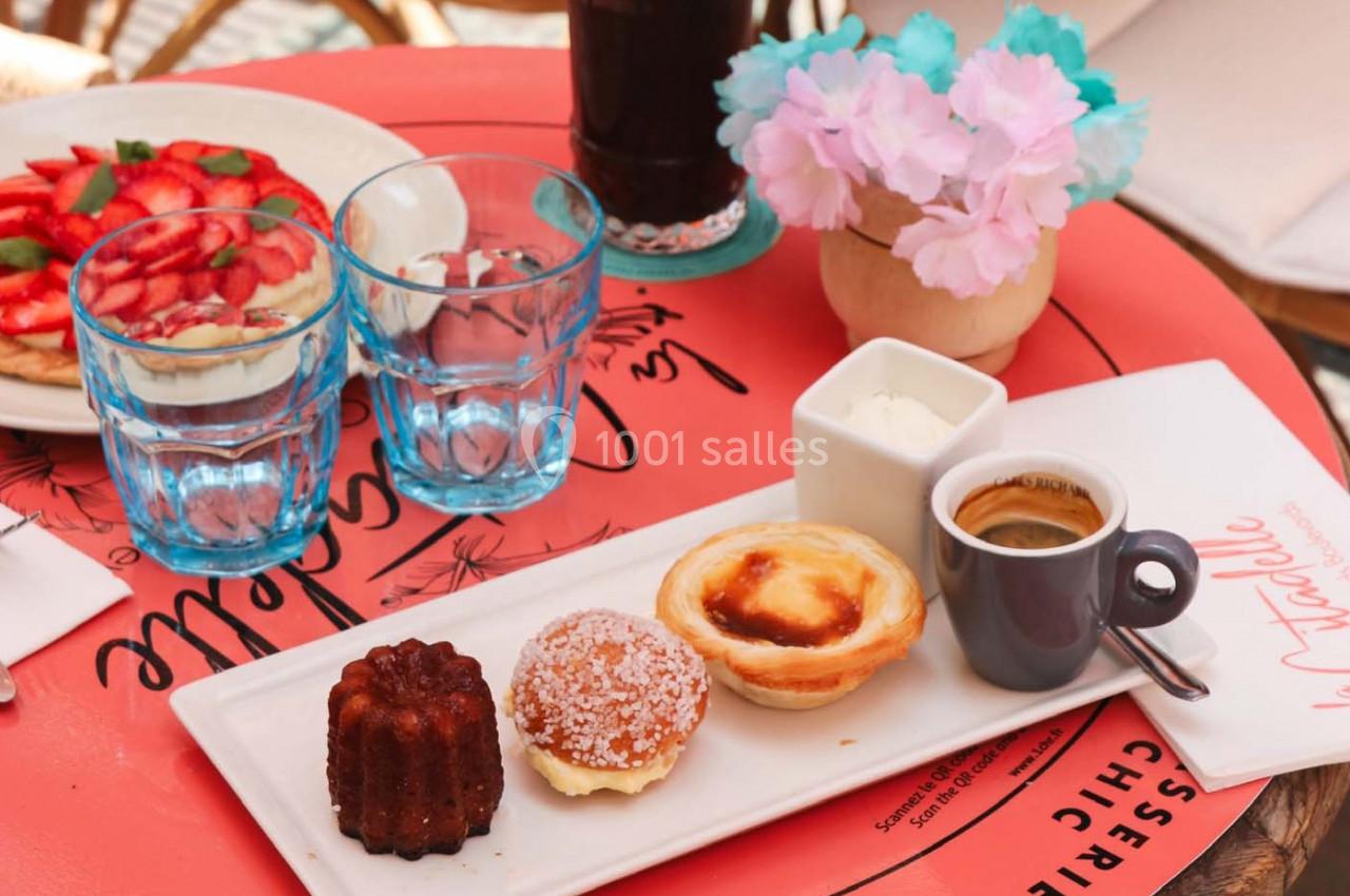Assiette de pâtisseries variées avec un café, posée sur une table rouge accompagnée de verres et d'une décoration florale.