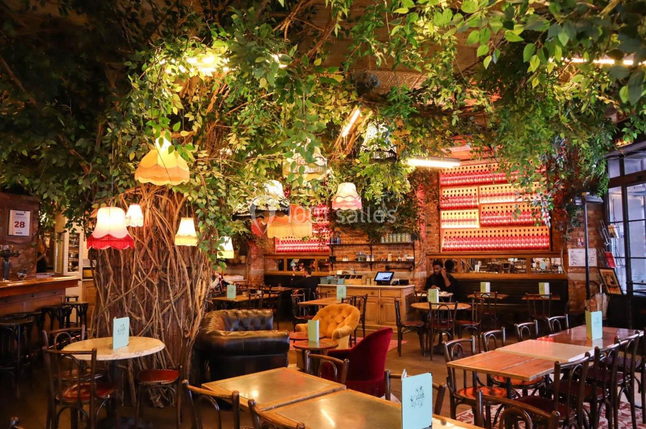 Salle de restaurant chaleureuse avec mobilier en bois, végétation suspendue et lampes vintage colorées.