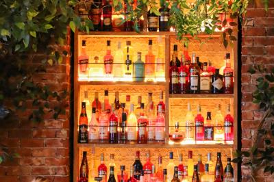 Étagères en bois remplies de bouteilles d'alcool, encadrées de briques et de feuillage, dans un décor de bar chaleureux.