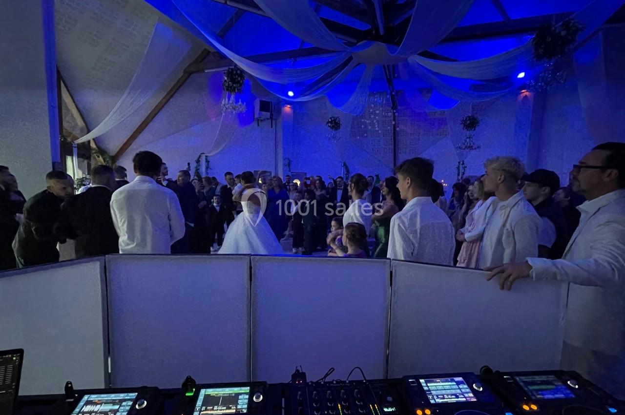 Salle de réception avec des invités en tenue de soirée, vue depuis une table de mixage éclairée par des lumières bleues.