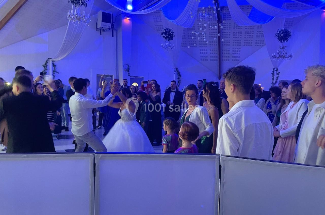 Groupe de personnes dansant lors d'une réception dans une salle décorée avec des drapés et un éclairage bleu.