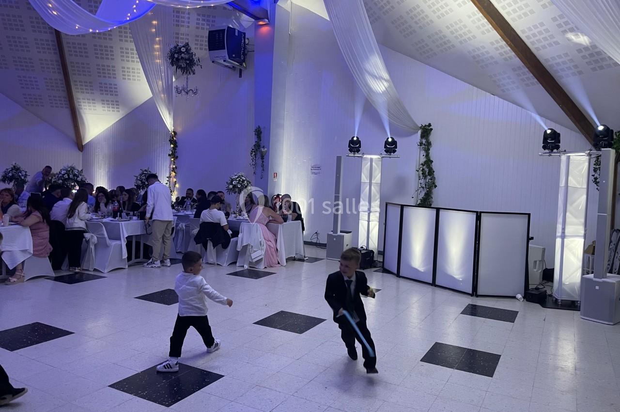Deux enfants en costume courant sur une piste de danse éclairée, lors d'une réception avec des invités assis.