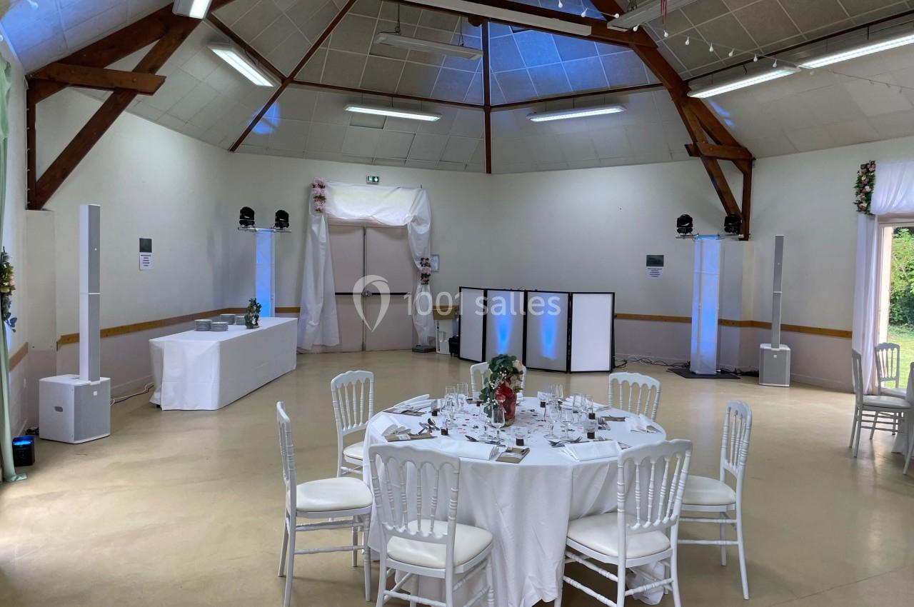 Salle de réception décorée avec des tables dressées, des chaises blanches et un éclairage discret.