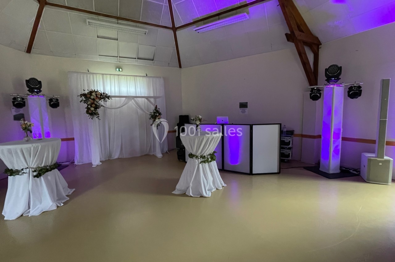 Salle décorée pour un événement avec tables hautes drapées, arche florale et éclairage violet.