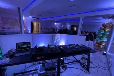 Équipement de DJ avec platines et ordinateur dans une salle éclairée en bleu, décorée de ballons et occupée par des invités.