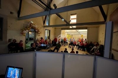 Un groupe de personnes assises dans une salle éclairée, décorée de ballons, regardant une projection.