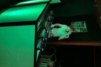 Un DJ mixe de la musique sur une table de mixage éclairée en vert dans une salle sombre.