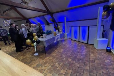 Salle décorée pour un événement avec ballons dorés et noirs, table dressée et éclairage bleu.