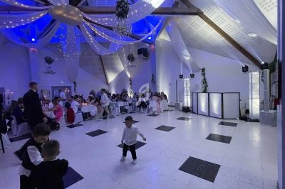 Salle de réception décorée avec des drapés et lumières, des invités assis à des tables et des enfants jouant au centre.