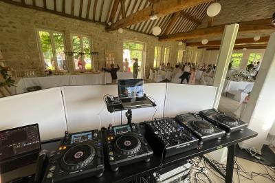 Poste de DJ avec platines et table de mixage dans une salle de réception lumineuse avec des invités en arrière-plan.