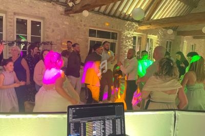 Des invités dansent et discutent dans une salle en pierre éclairée par des lumières colorées, vue depuis une table de DJ.