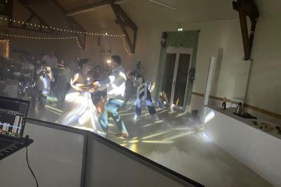 Un couple danse sous des jeux de lumière et de la fumée dans une salle de réception avec des invités en arrière-plan.