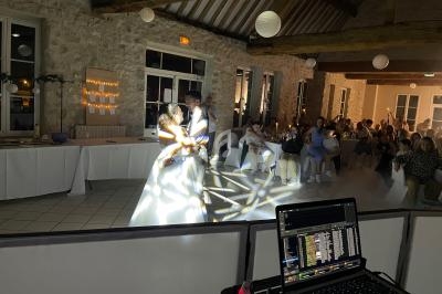 Un couple danse sous des jeux de lumière dans une salle en pierre, avec des invités assis en arrière-plan.