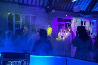 Personnes dansant et discutant dans une salle éclairée par des lumières colorées, avec un DJ en arrière-plan.
