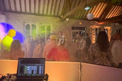 Des personnes dansent dans une salle en pierre éclairée par des lumières colorées, avec une table de mixage au premier plan.