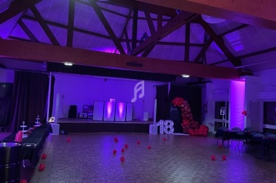 Salle décorée pour une fête avec éclairage violet, ballons rouges formant le chiffre 18 et espace de danse dégagé.
