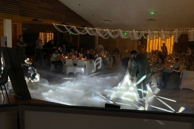 Un couple danse au milieu d'une salle éclairée, entourée d'invités assis et d'une ambiance lumineuse tamisée.