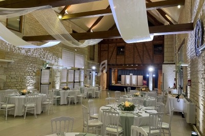 Salle de réception décorée avec des tables rondes, nappes blanches, chaises en bois et voilages suspendus au plafond.