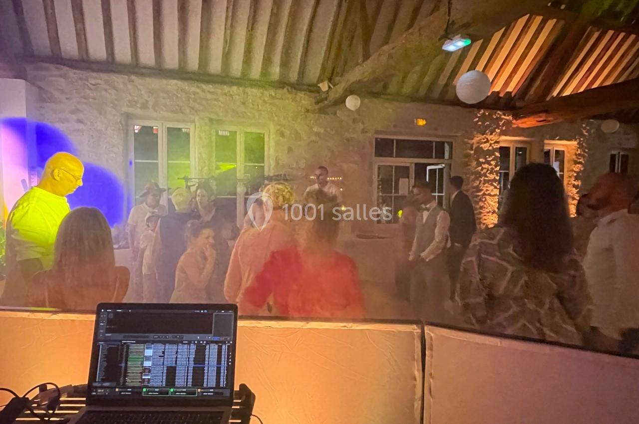 Des personnes dansent dans une salle en pierre éclairée par des lumières colorées, avec une table de mixage au premier plan.