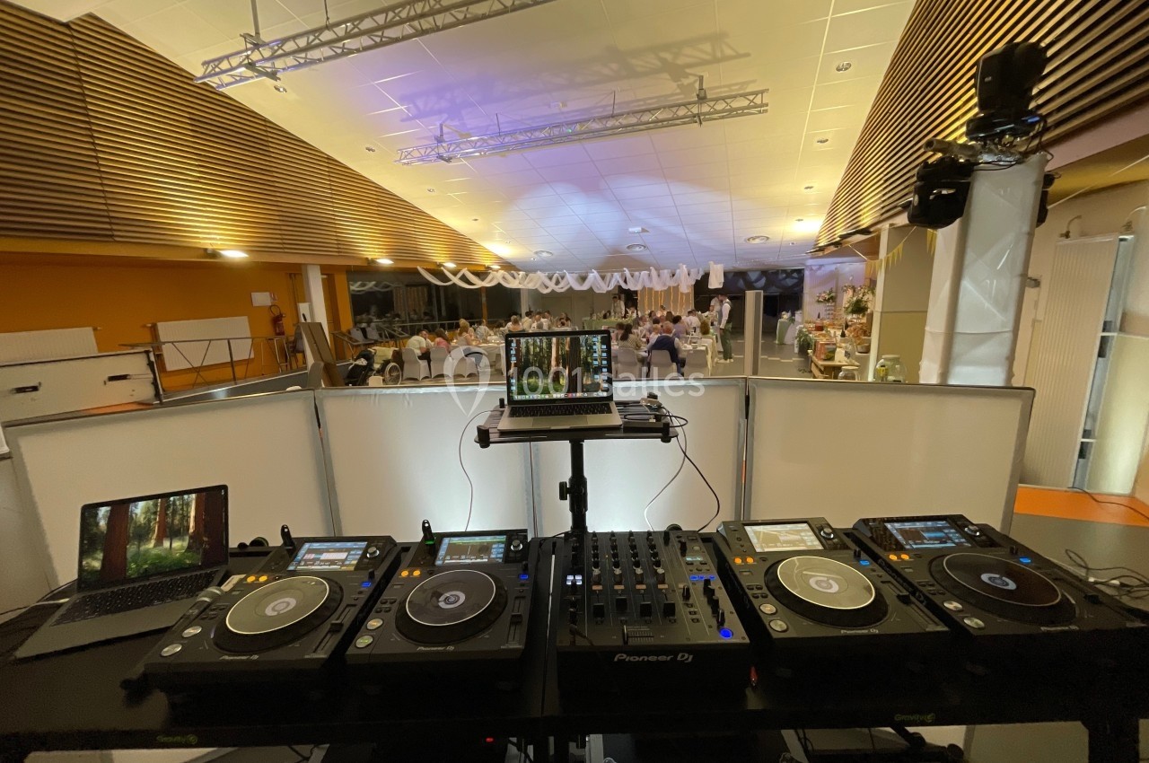 Poste de DJ avec platines et ordinateur dans une salle de réception éclairée, décorée pour un événement.