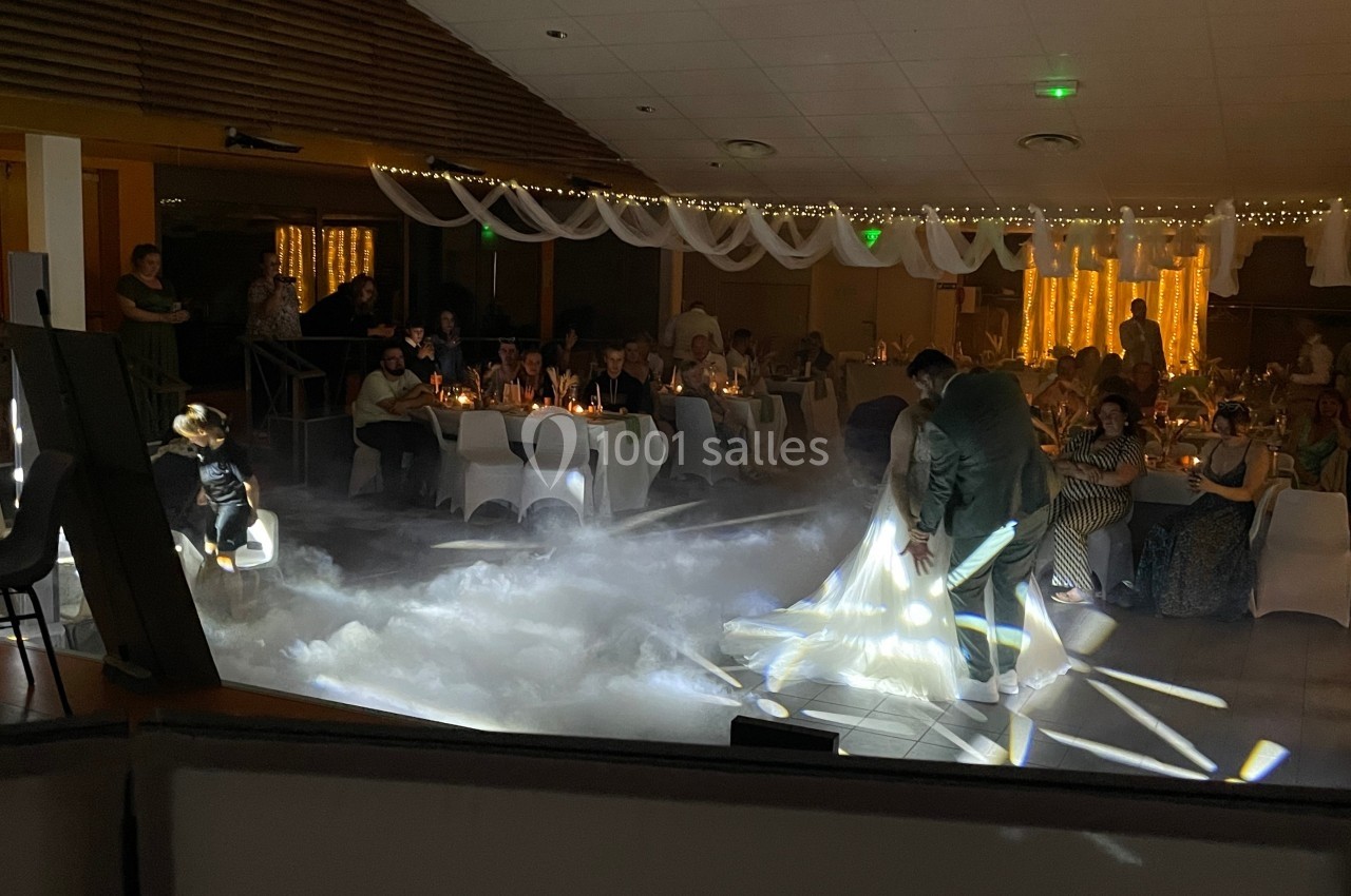 Un couple danse au milieu d'une salle éclairée, entourée d'invités assis et d'une ambiance lumineuse tamisée.